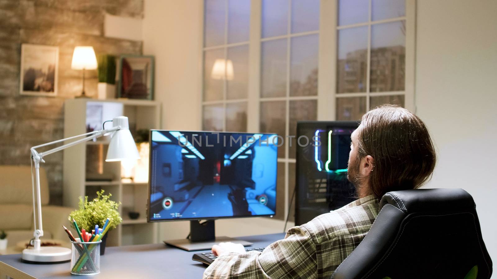 Excited young gamer with long hair sitting on gaming chair. Man using computer for gaming.