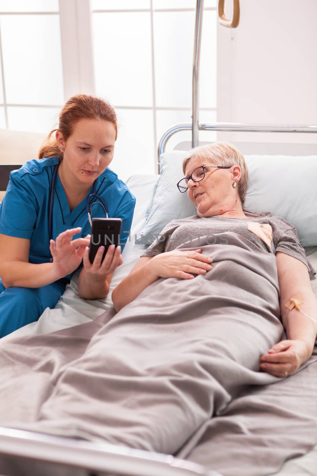 Female doctor using phone in nursing home for senior woman.