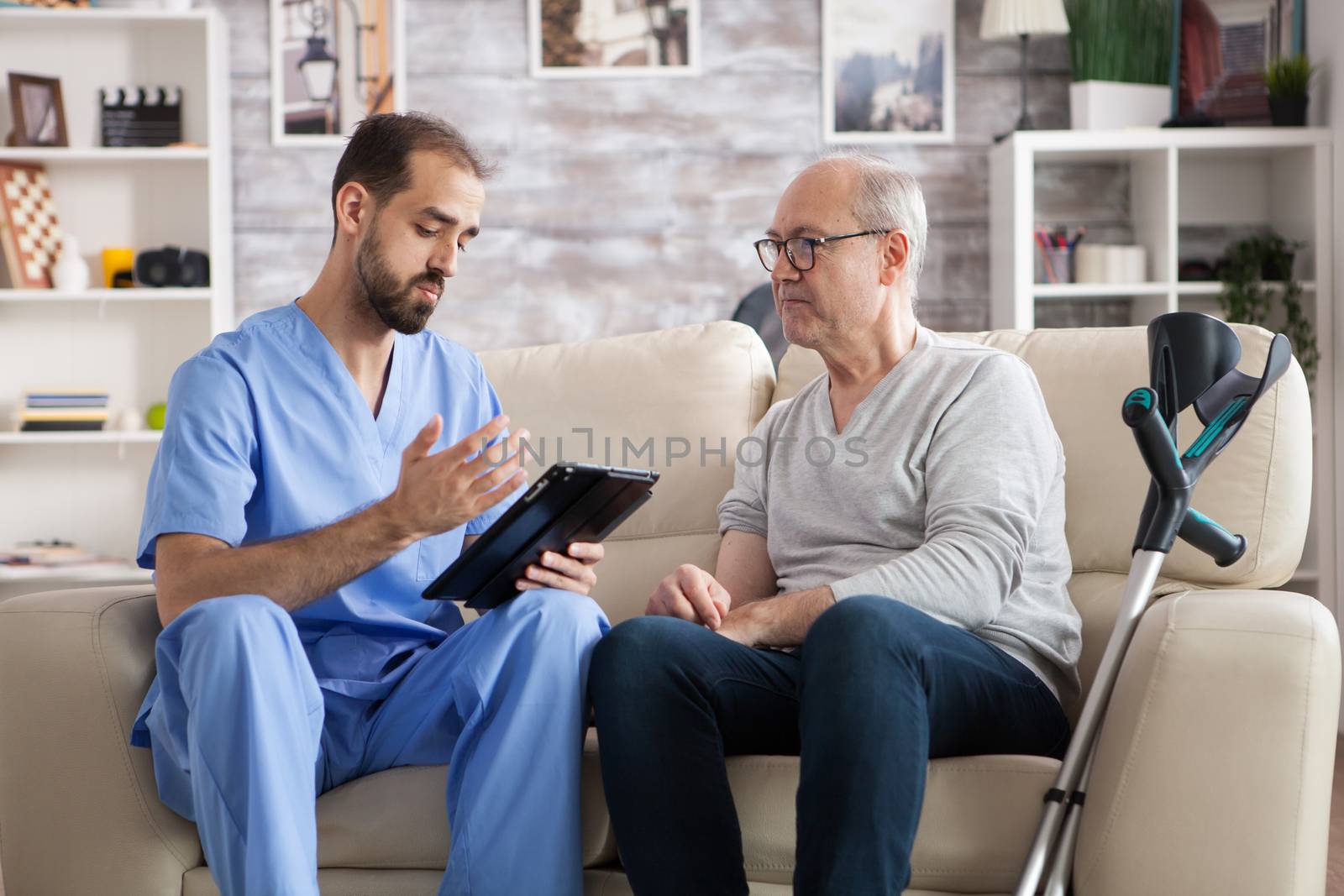 Young doctor in nursing home checking elderly age man treatment on tablet computer.