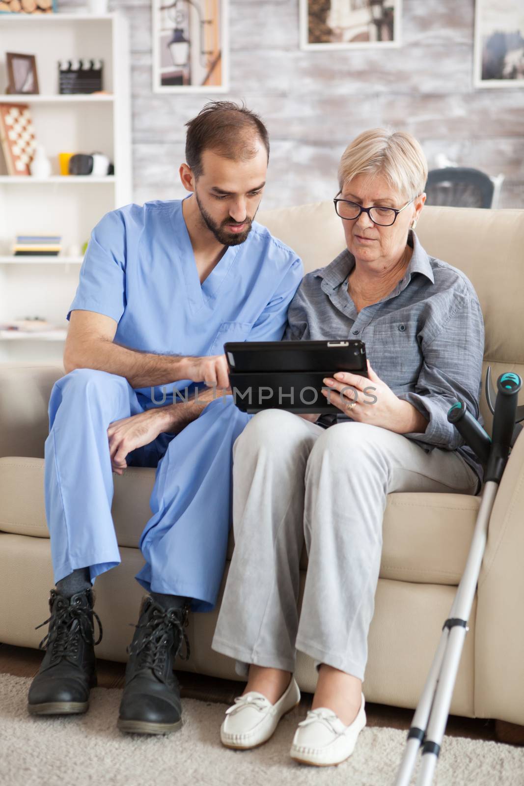 Young doctor reading diagnostic on tablet for senior woman in nursing home.