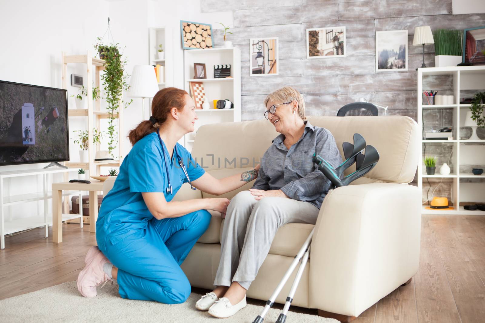 Cheerful old woman sitting on couch in a a nursing home talking with her health visitor. Crutches on the couch.
