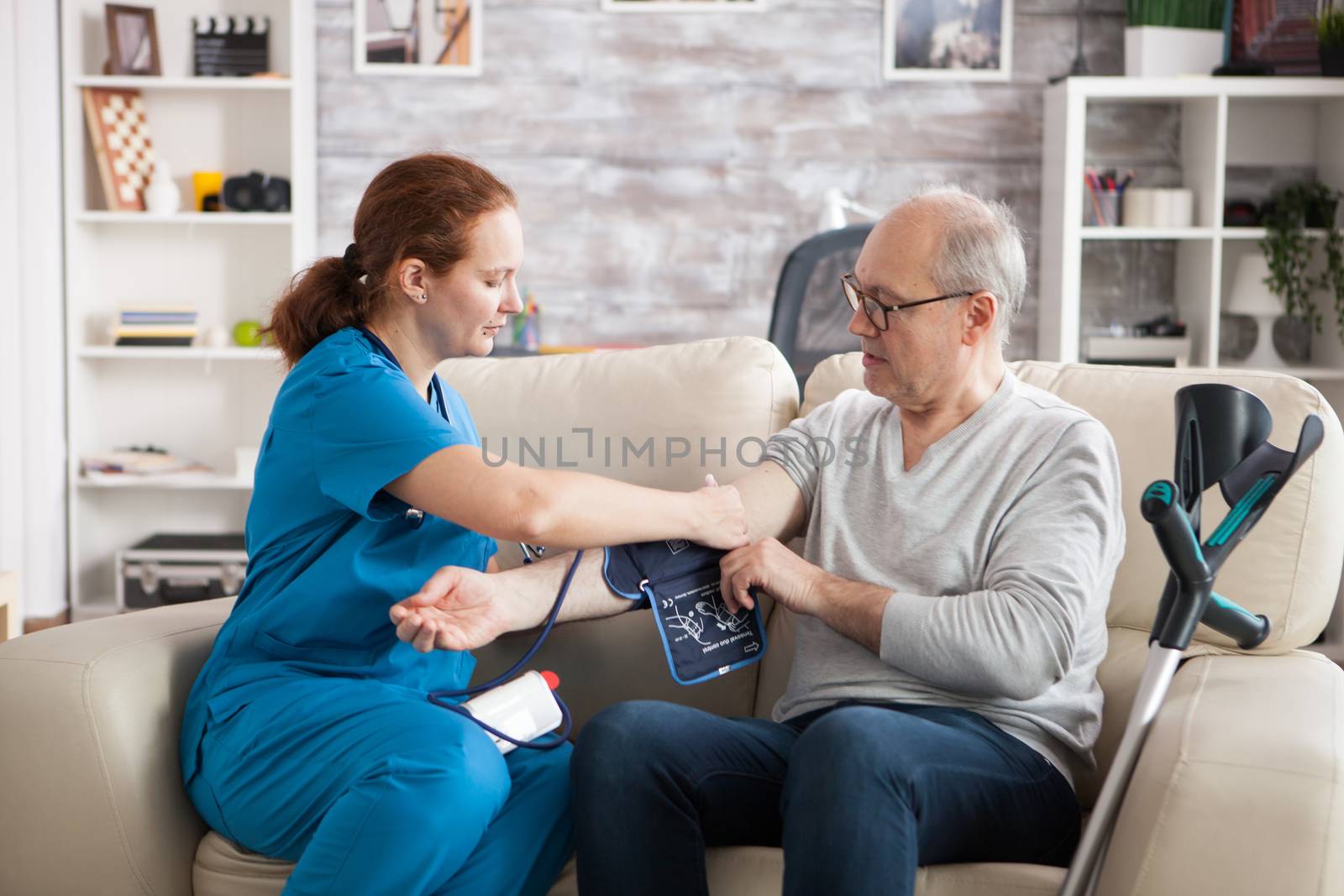 Young doctor in nursing home taking digital blood pressure of old man.