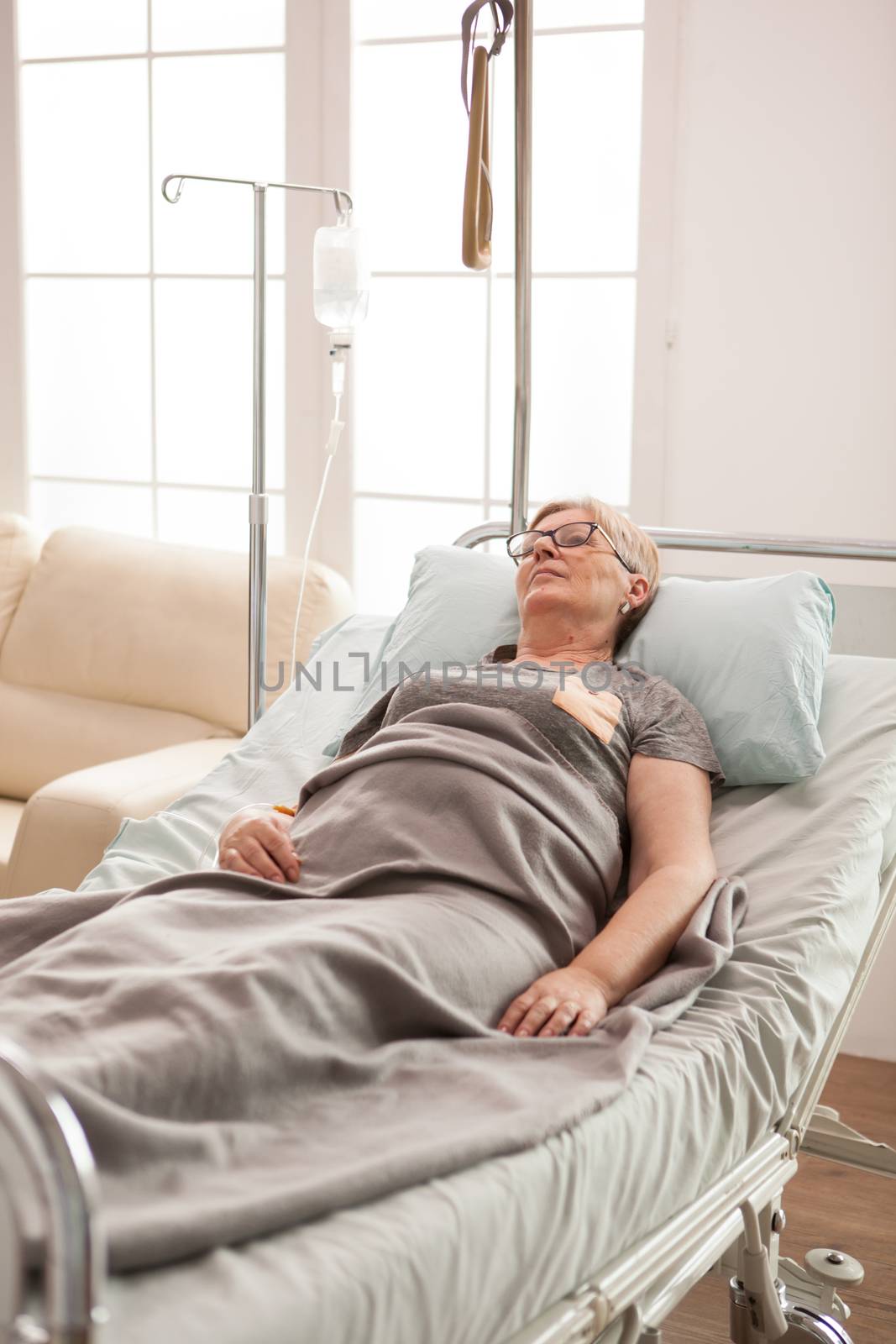Mature lonely woman laying on bed in a nursing home covered with a blanket.