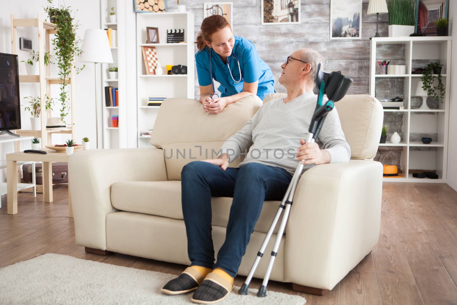 Old man sitting on couch holding his crutches by DCStudio