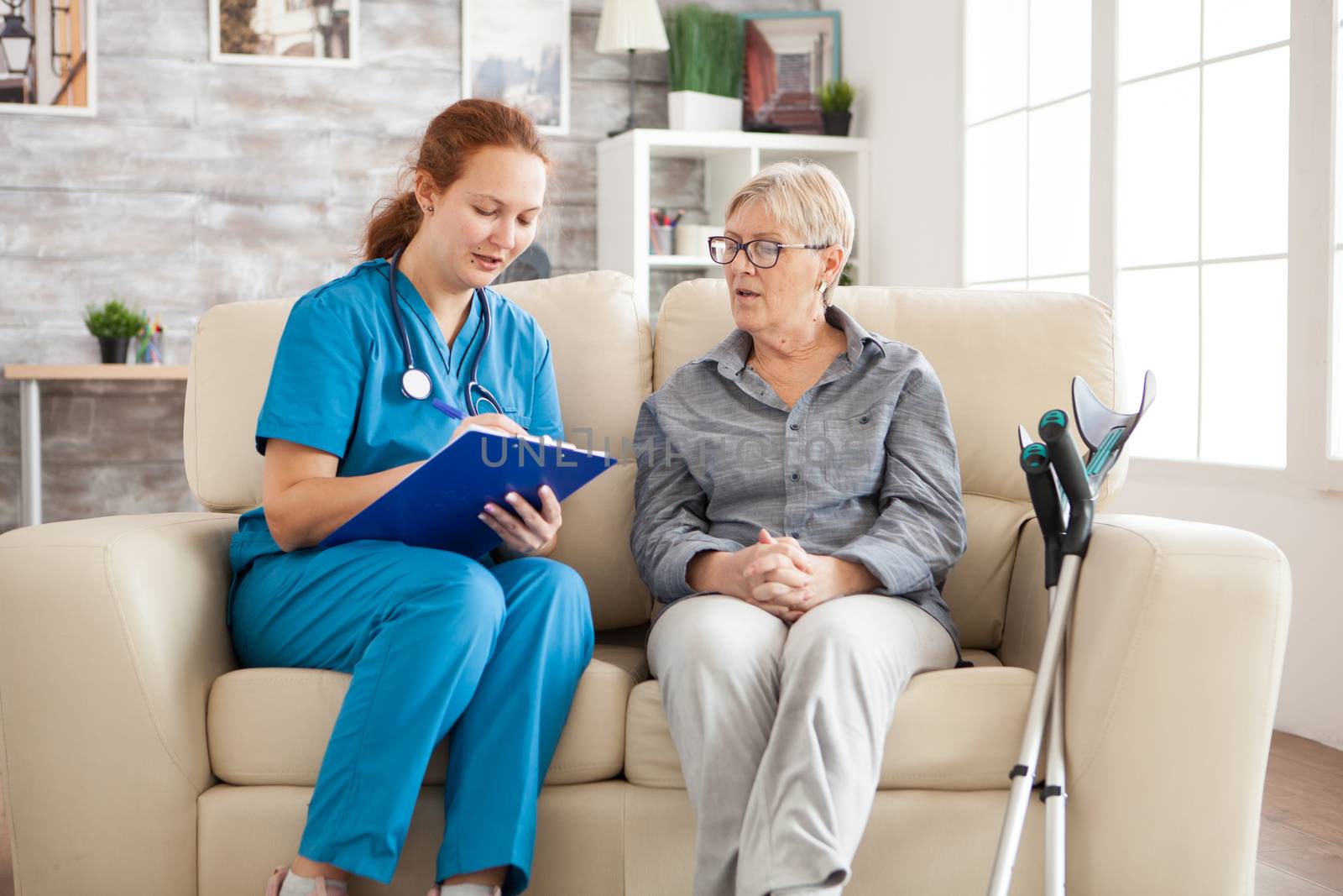 Female doctor in nursing home doing survey on senior woman by DCStudio