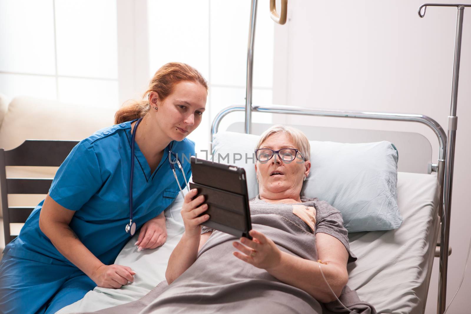 Portrait of old woman in nursing home using tablet computer. Female nurse with retired woman.