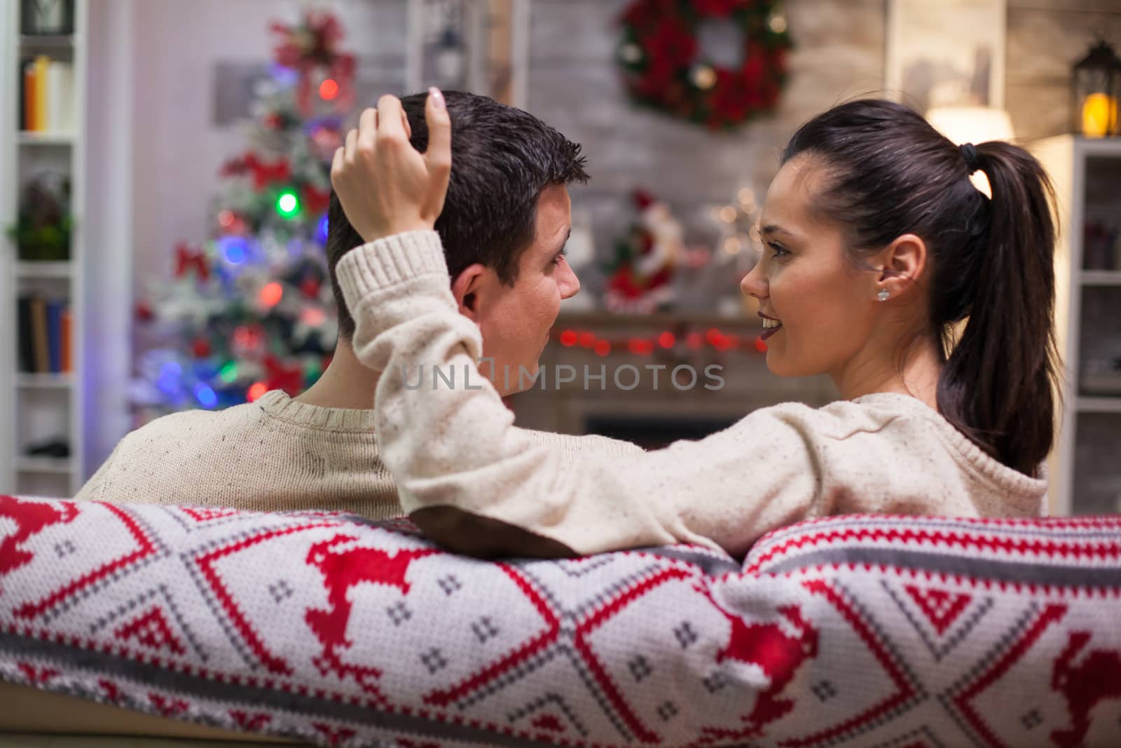 Back view of young woman sitting on couch on christmas day in front of fireplace.