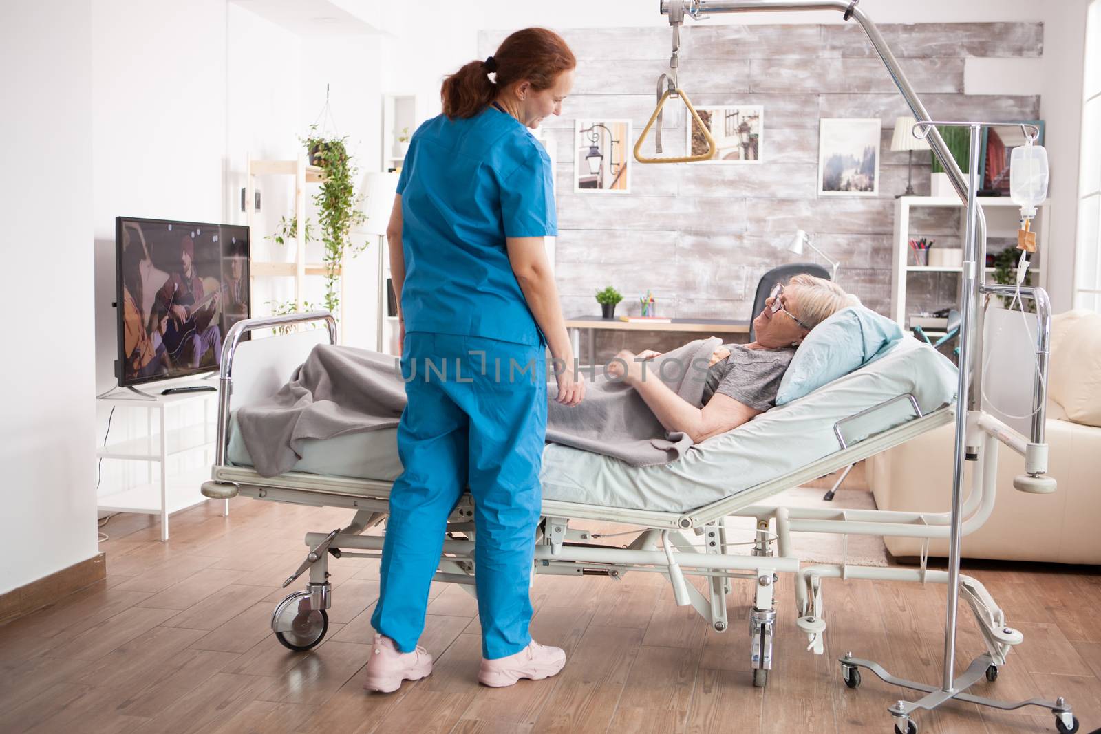 Old woman in nursing home smiling at female caretaker. Old woman laying on bed.