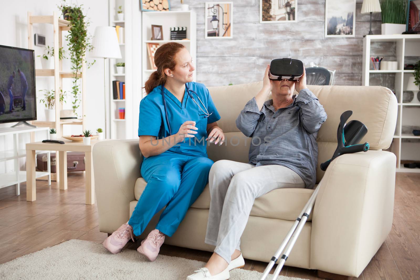 Female doctor looking at old woman in nursing home experiencing virtual reality with vr headset.