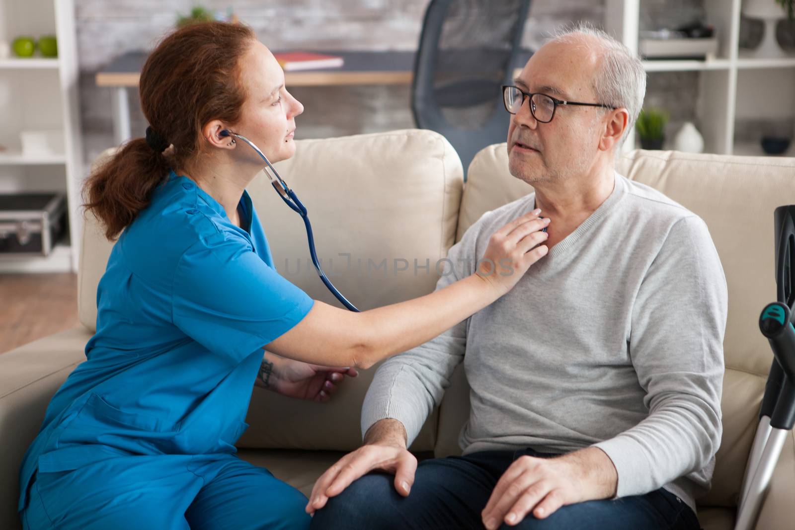 Pretty female nurse using stethoscope to listen the heart of old man in nursing home.