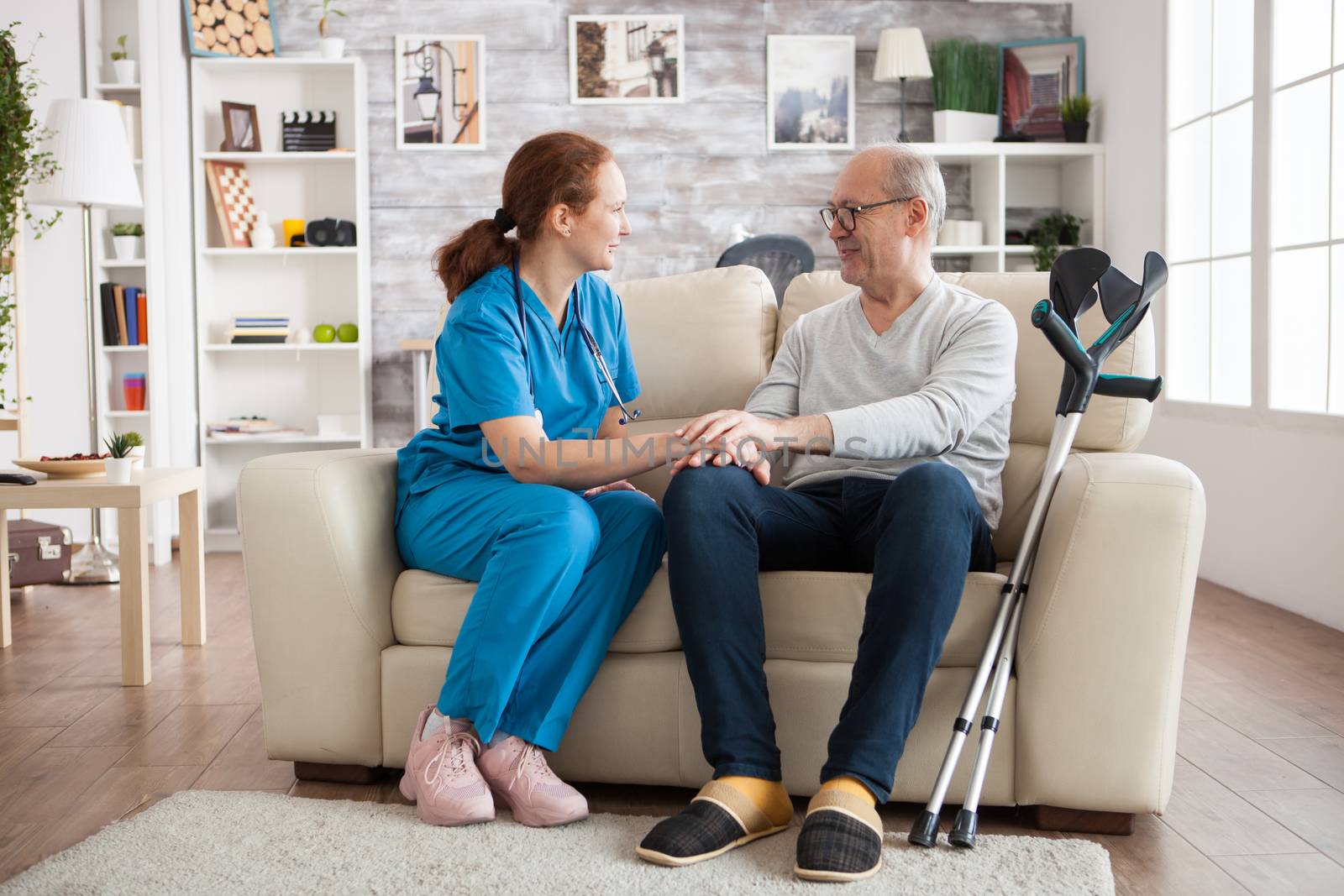 Female doctor and senior man smiling to each other while sitting on couch in nursing home.