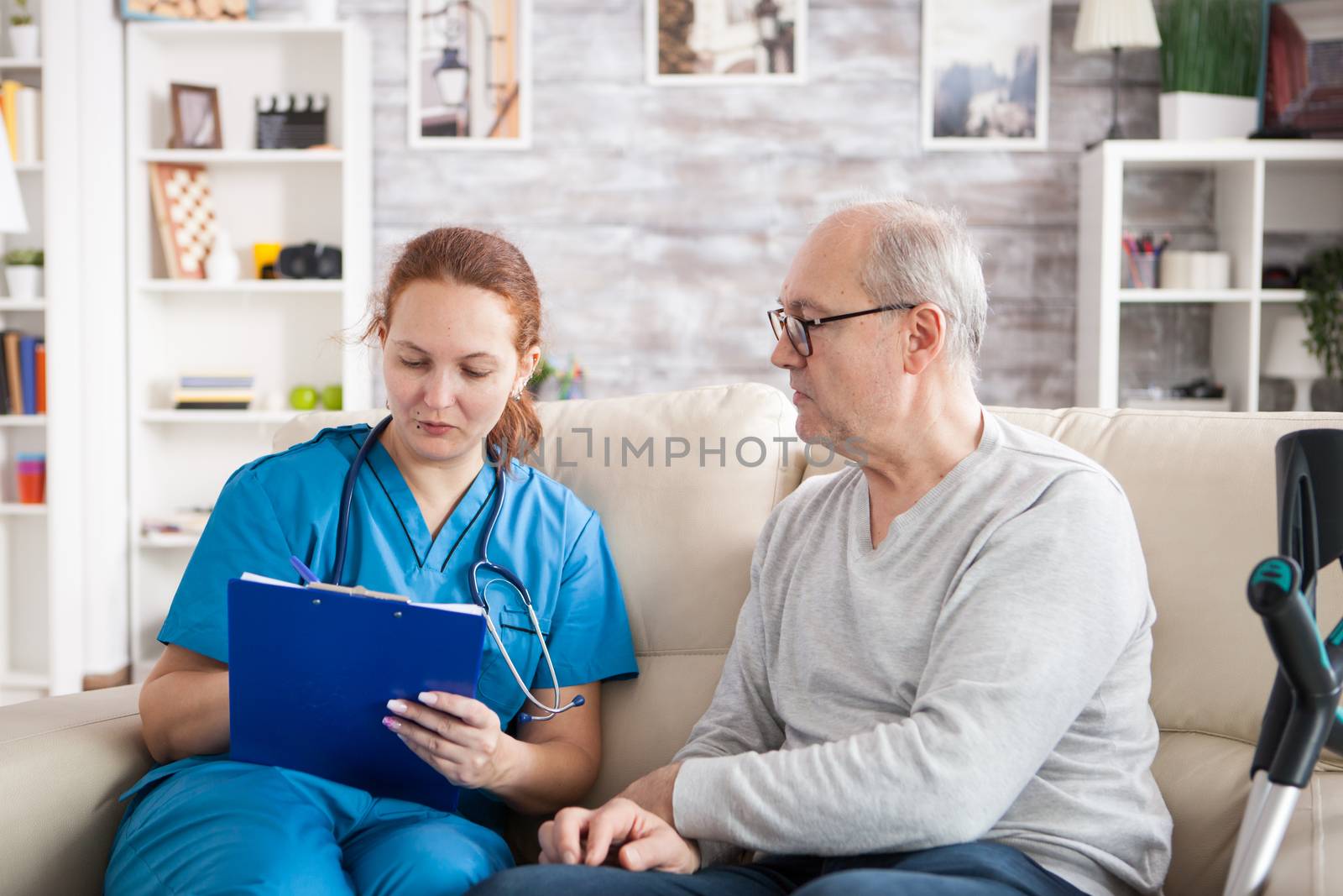 Female doctor with senior man sitting on couch in nursing home writing a prescription on clipboard.