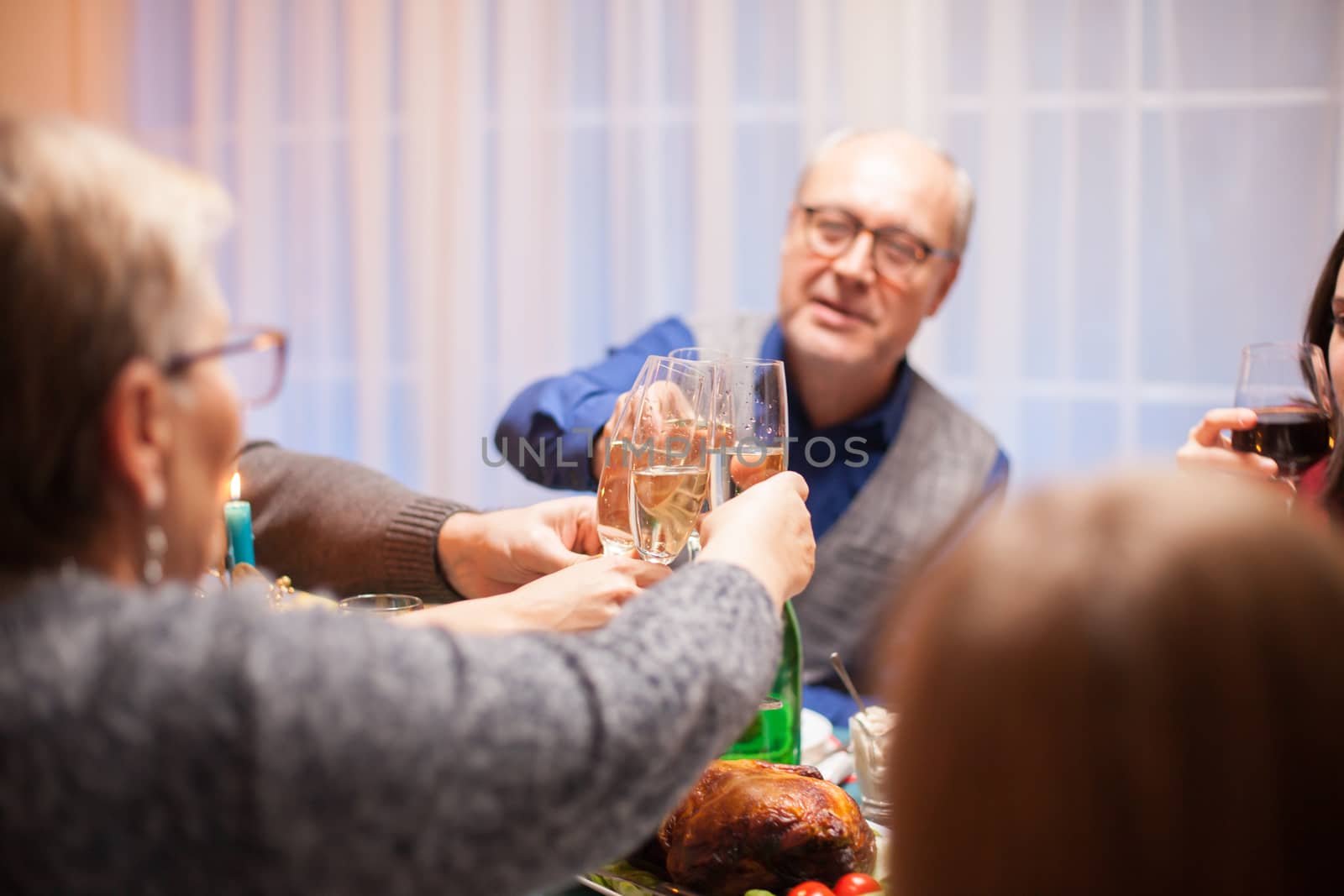 Senior man clinking a glass of wine with his family at christmas celebration.