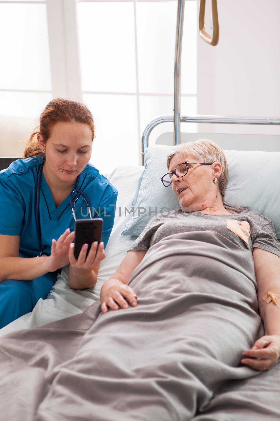 Female doctor helping old woman sitting on bed by DCStudio