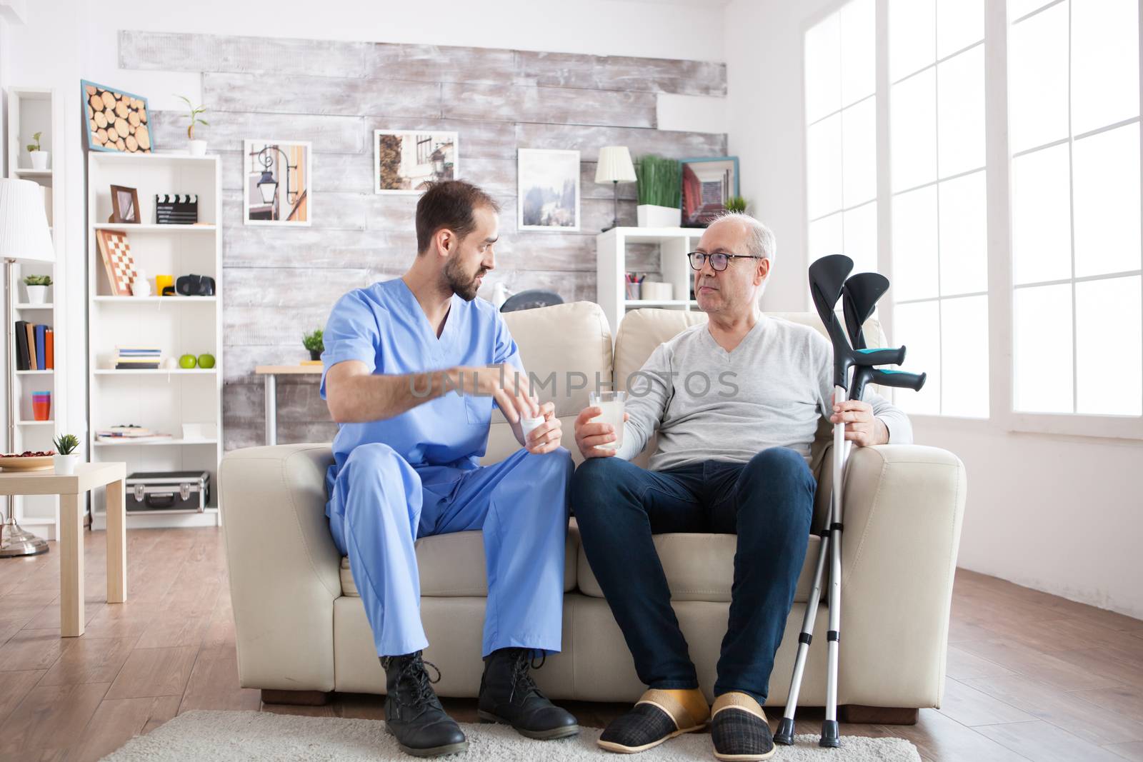 Young male nurse in nursing home with pills for senior man by DCStudio