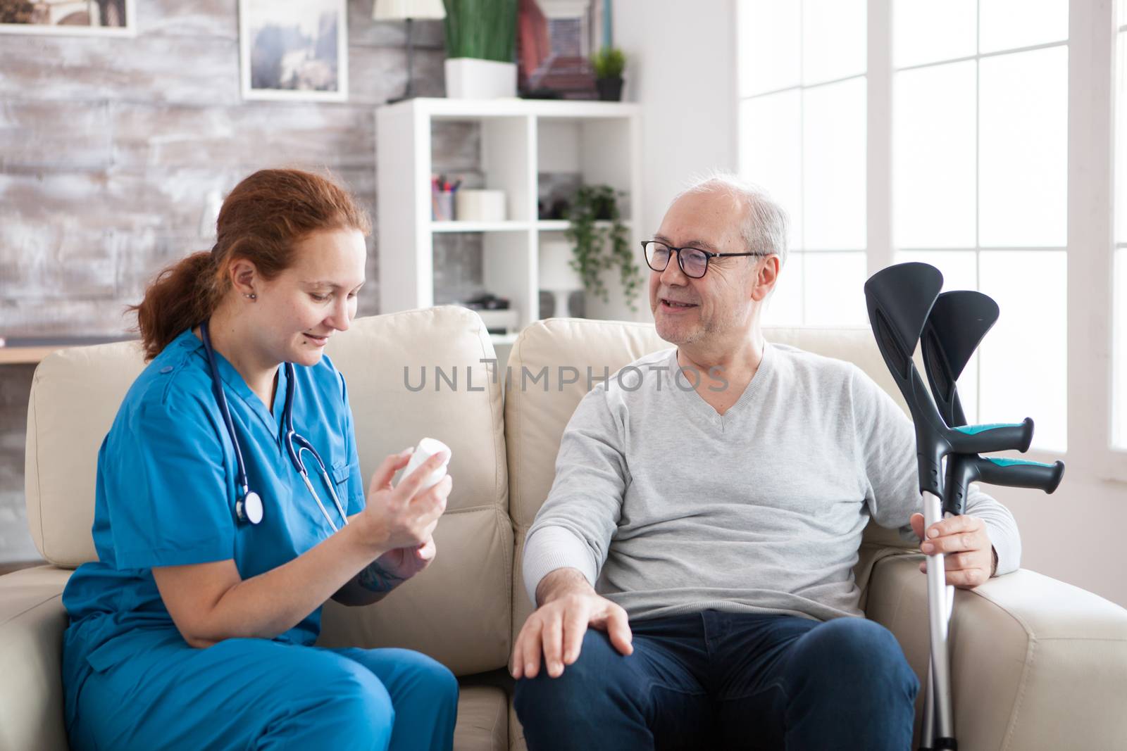 Female doctor in nursing home sitting on couch holding pills by DCStudio