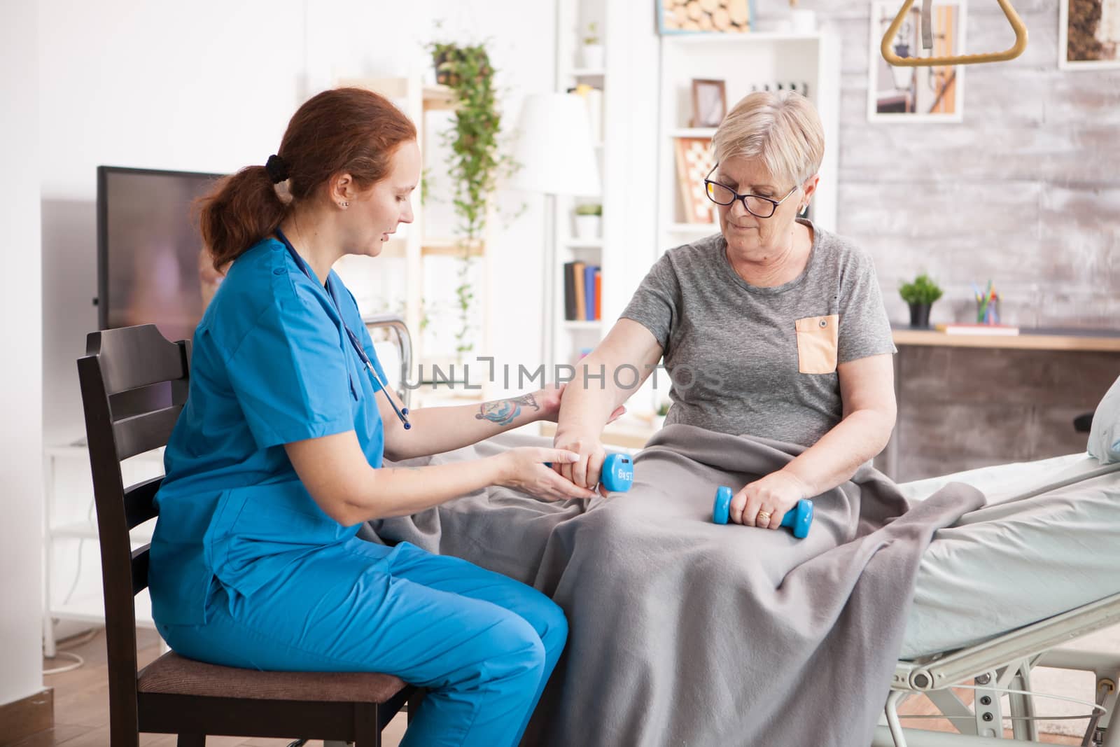 Senior woman sitting on bed in nursing home doing physiotherapy by DCStudio