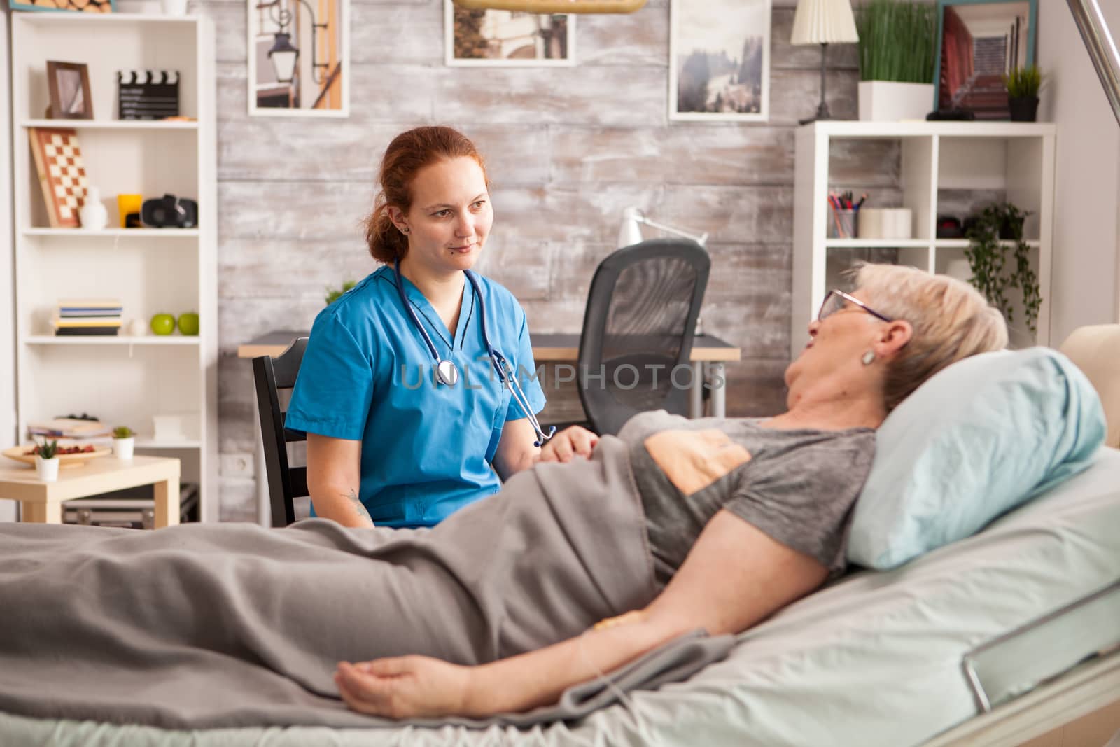 Female assistant sitting on a chair next to a sick woman in a nursing home.