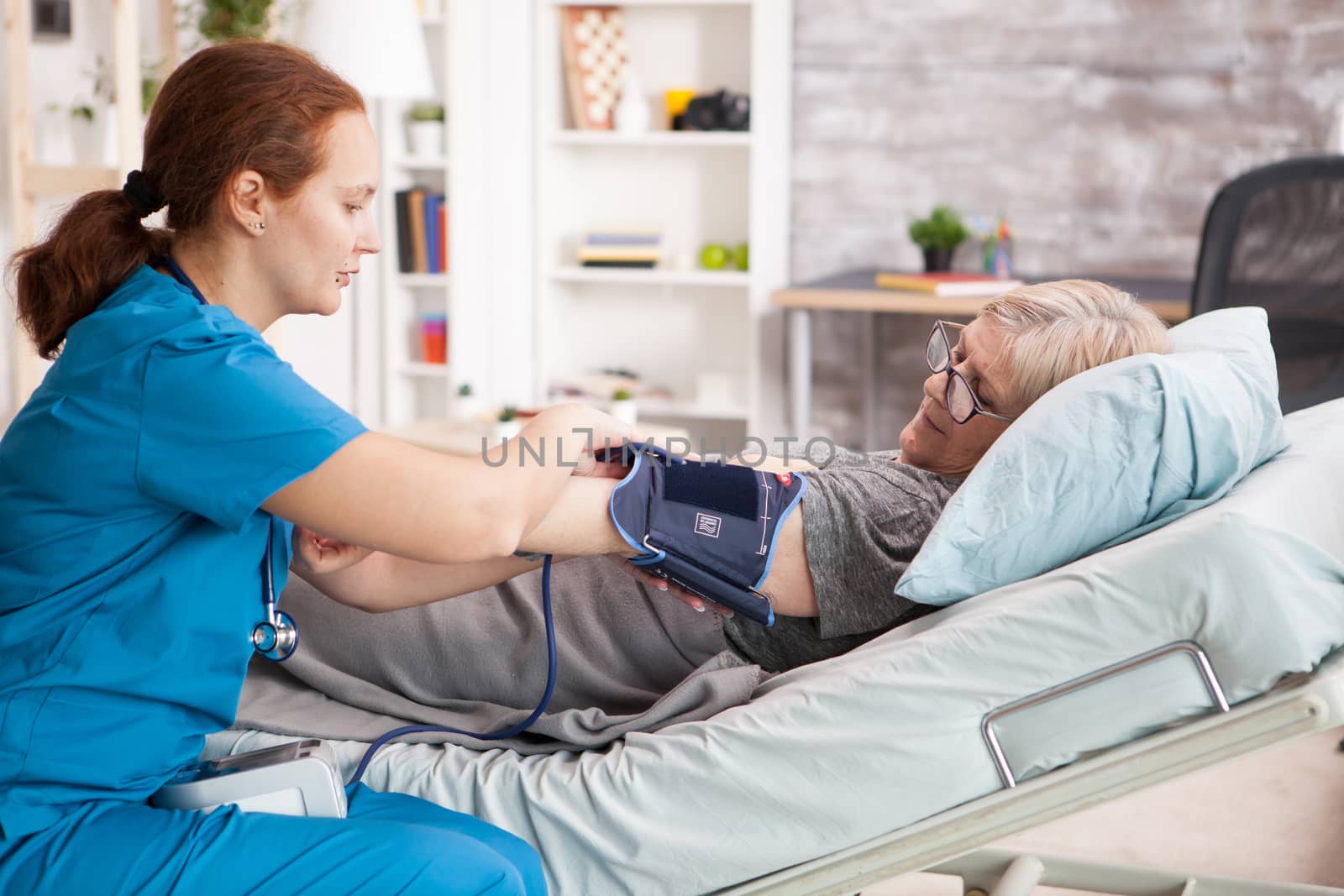 Female doctor in nursing home measuring blood pressure of senior woman laying in bed.