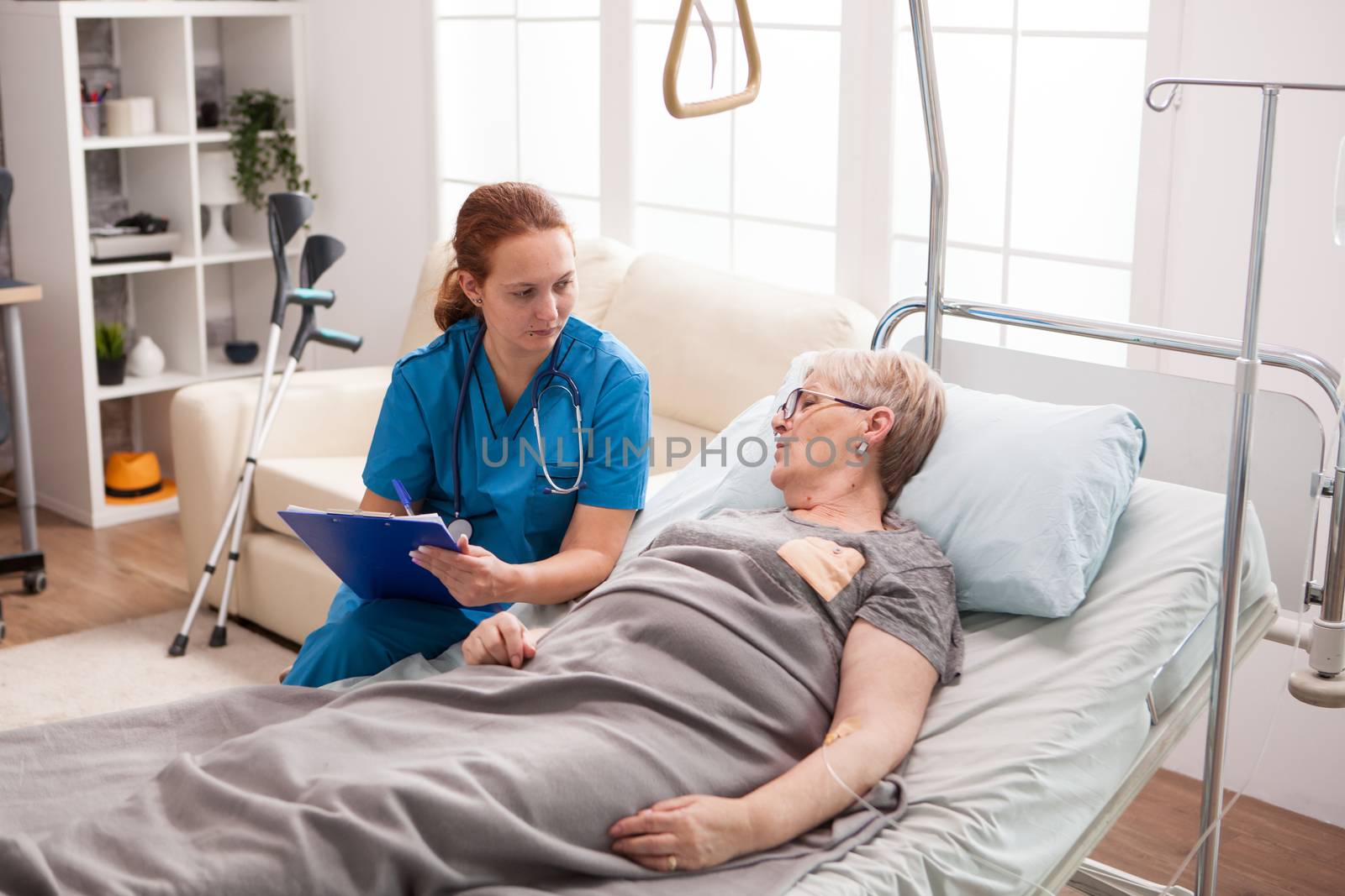 Female caregiver with cliboard talking with sick woman in nursing home.