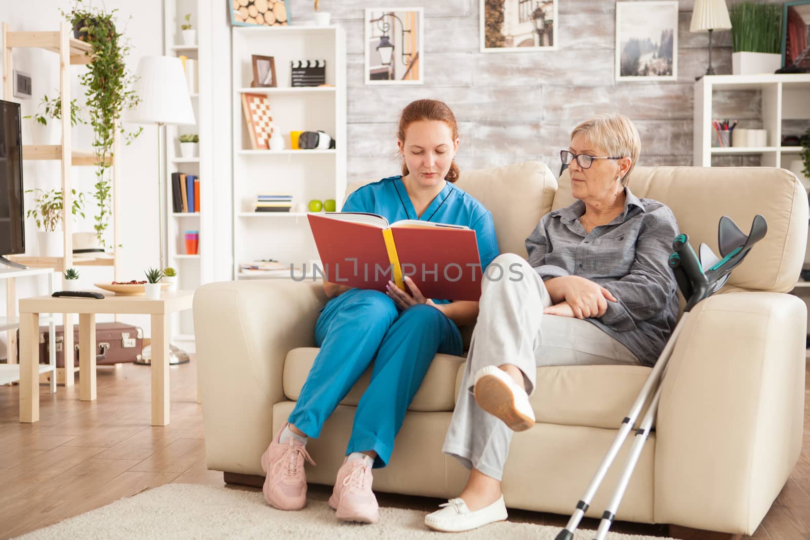 Doctor with blue uniform reading a book for senior woman in retirement home.