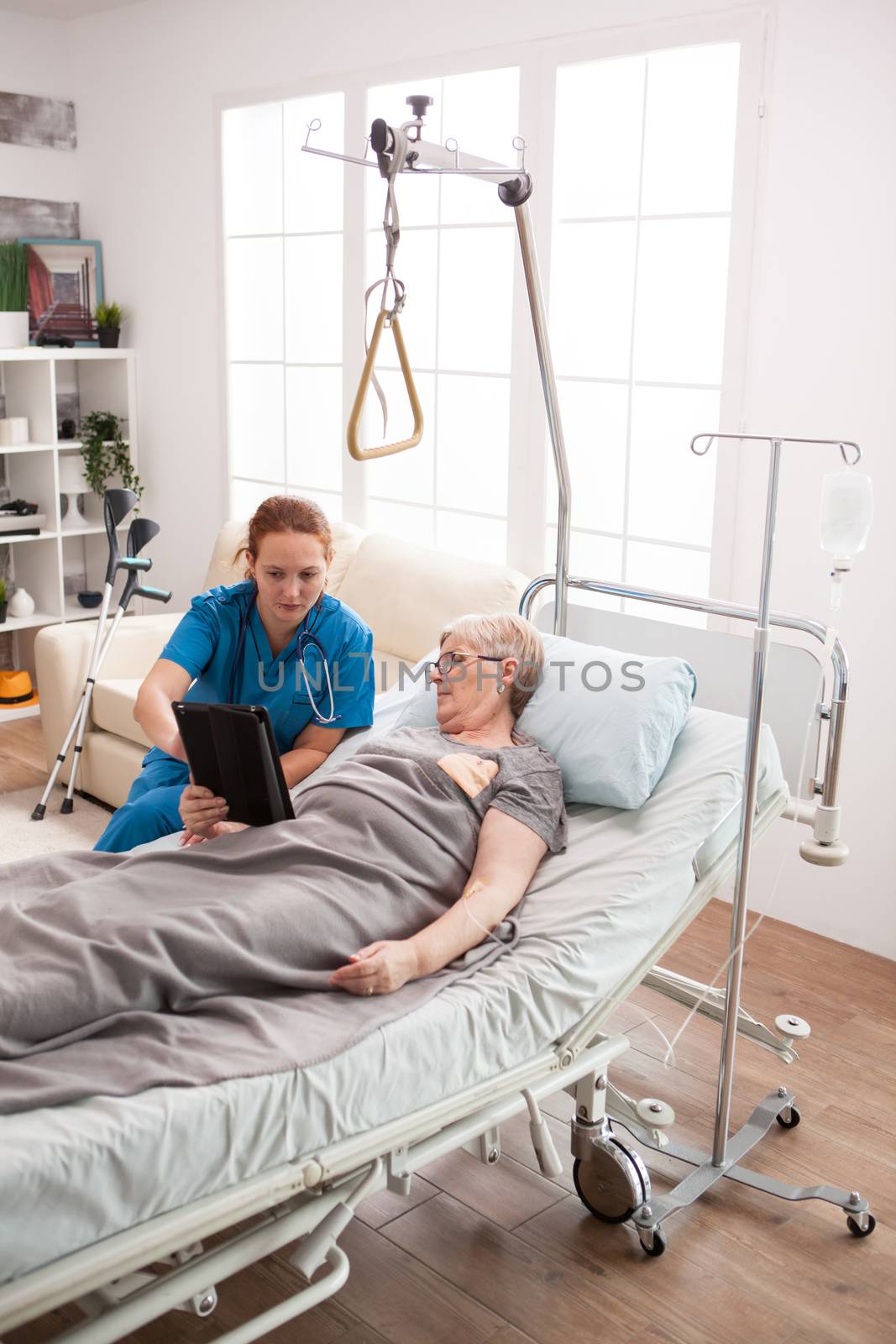 Female caretaker and senior woman using tablet computer in nursing home.