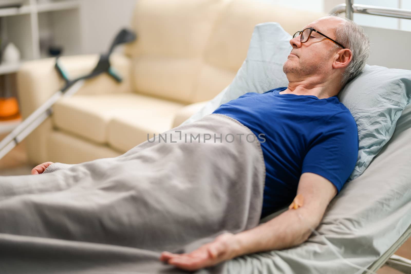 Senior man lying in nursing home with cannula on his arm.