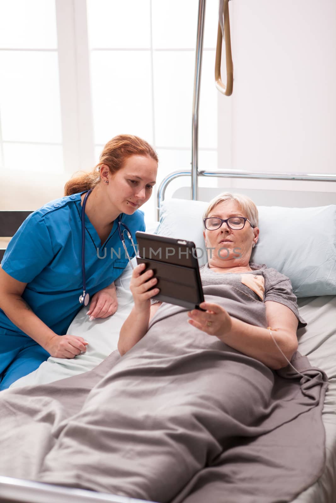 Young doctor and senior woman in nursing home using tablet to read medical results.