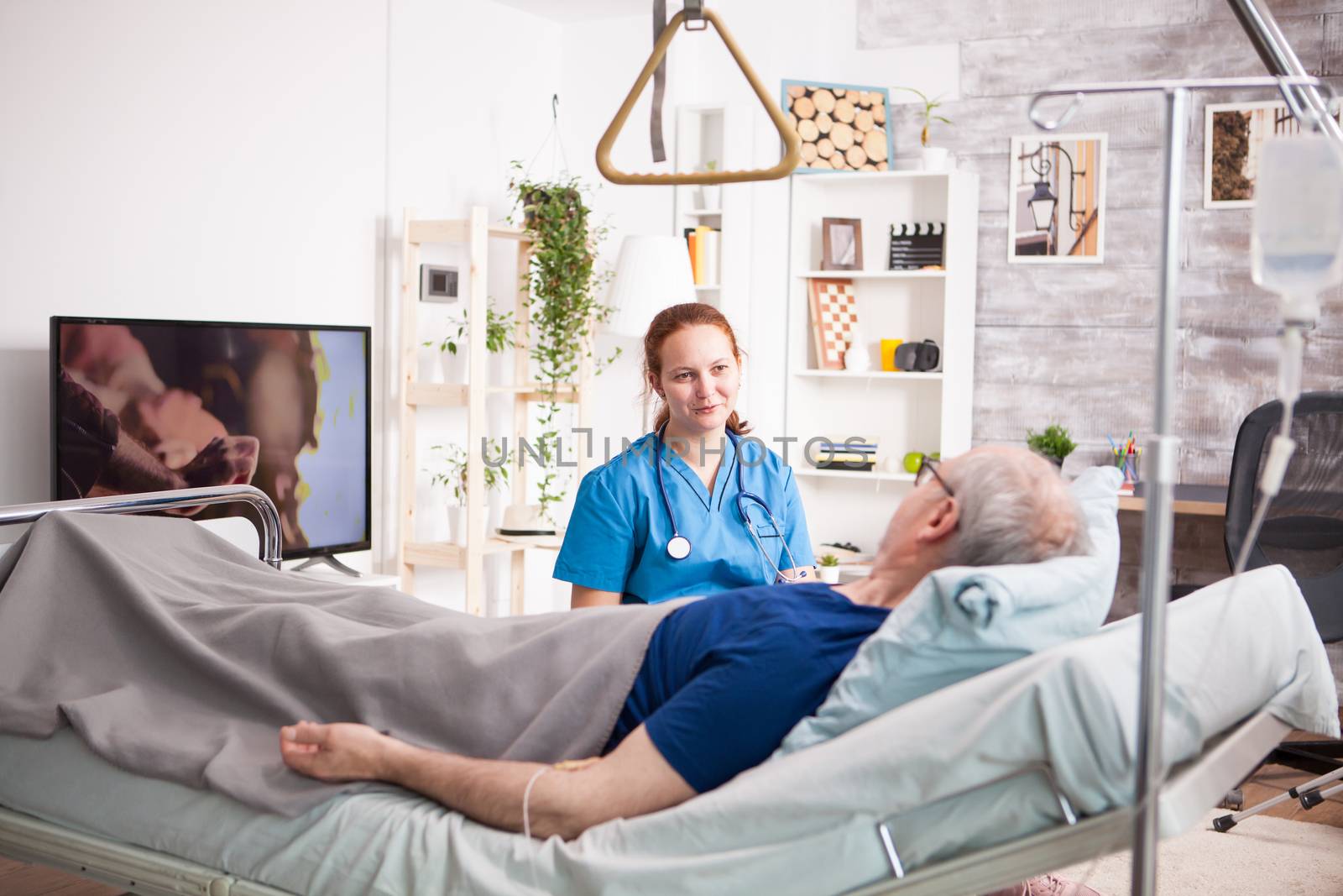 Sick old man laying on bed in nursing home and talking with female nurse.