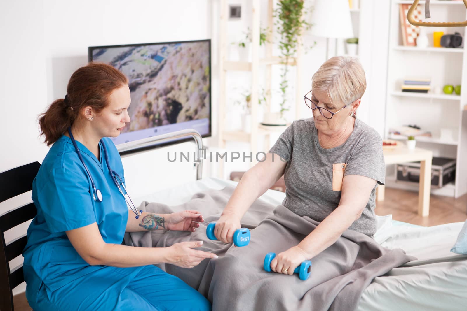 Health visitor helping old woman in nursing home to do her physiotherapy using dumbbells.