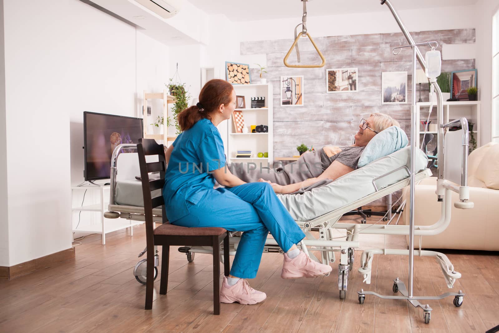 Female nurse in nursing home checking sick old woman lying in bed.