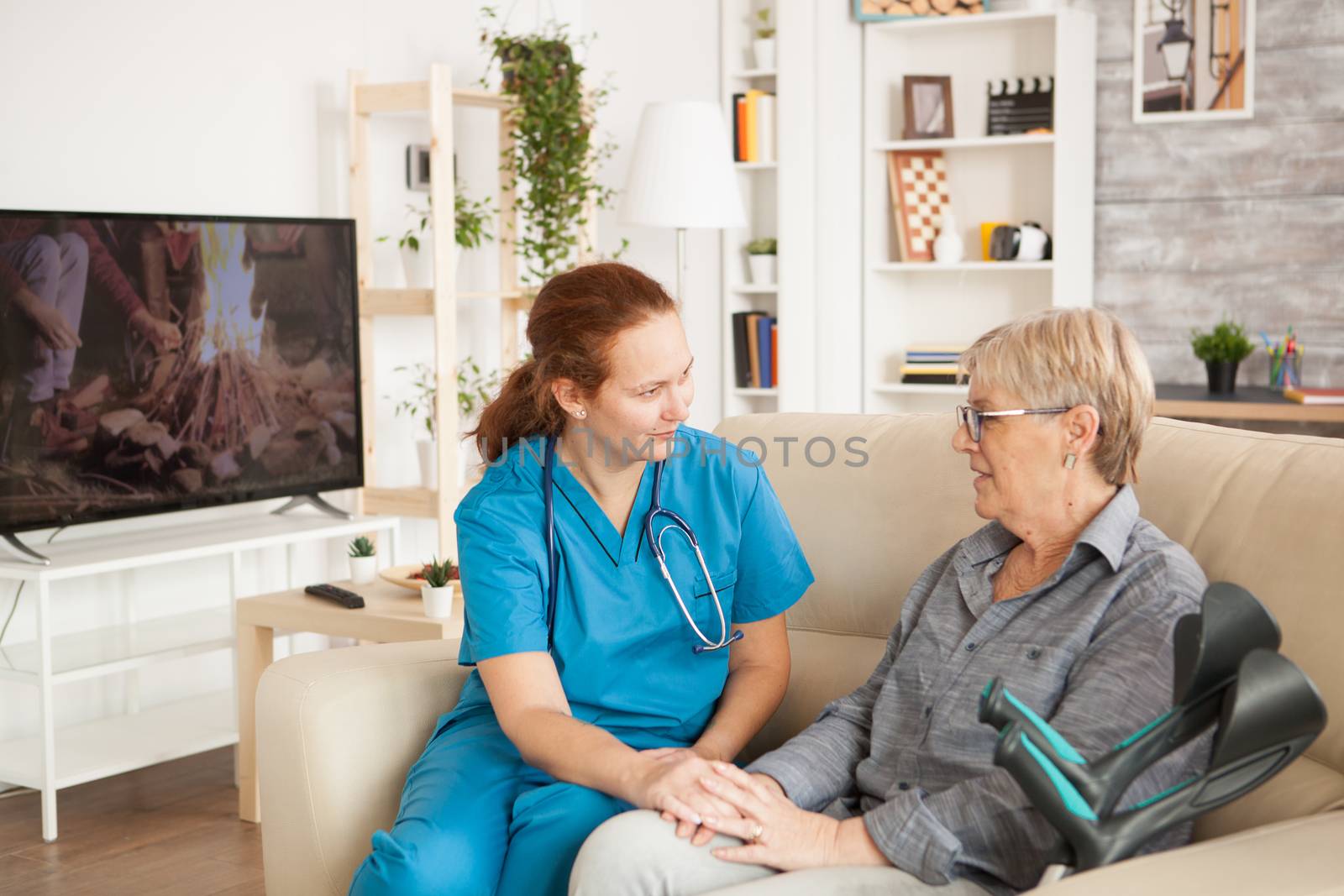 Female assistant talking with senior woman in nursing home with crutches.