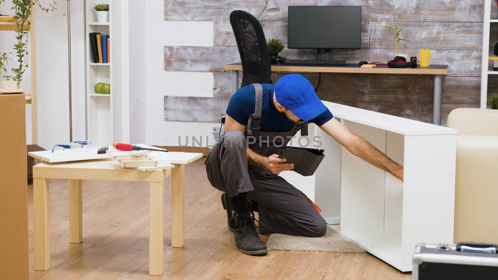 Male worker using modern technology for furniture assembly in a new home. Worker with tablet computer.