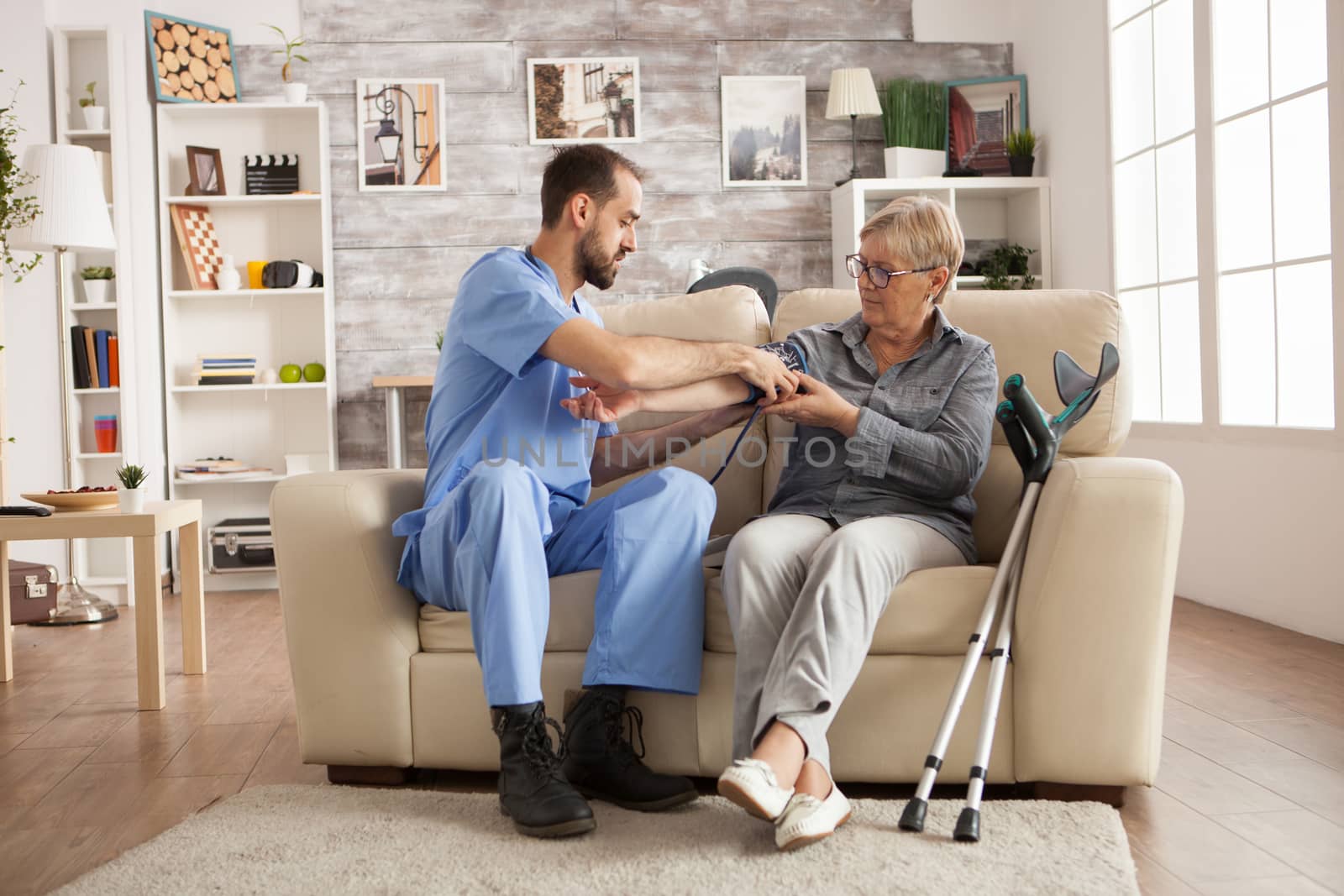 Male nurse using digital blood pressure device on senior woman in nursing home.