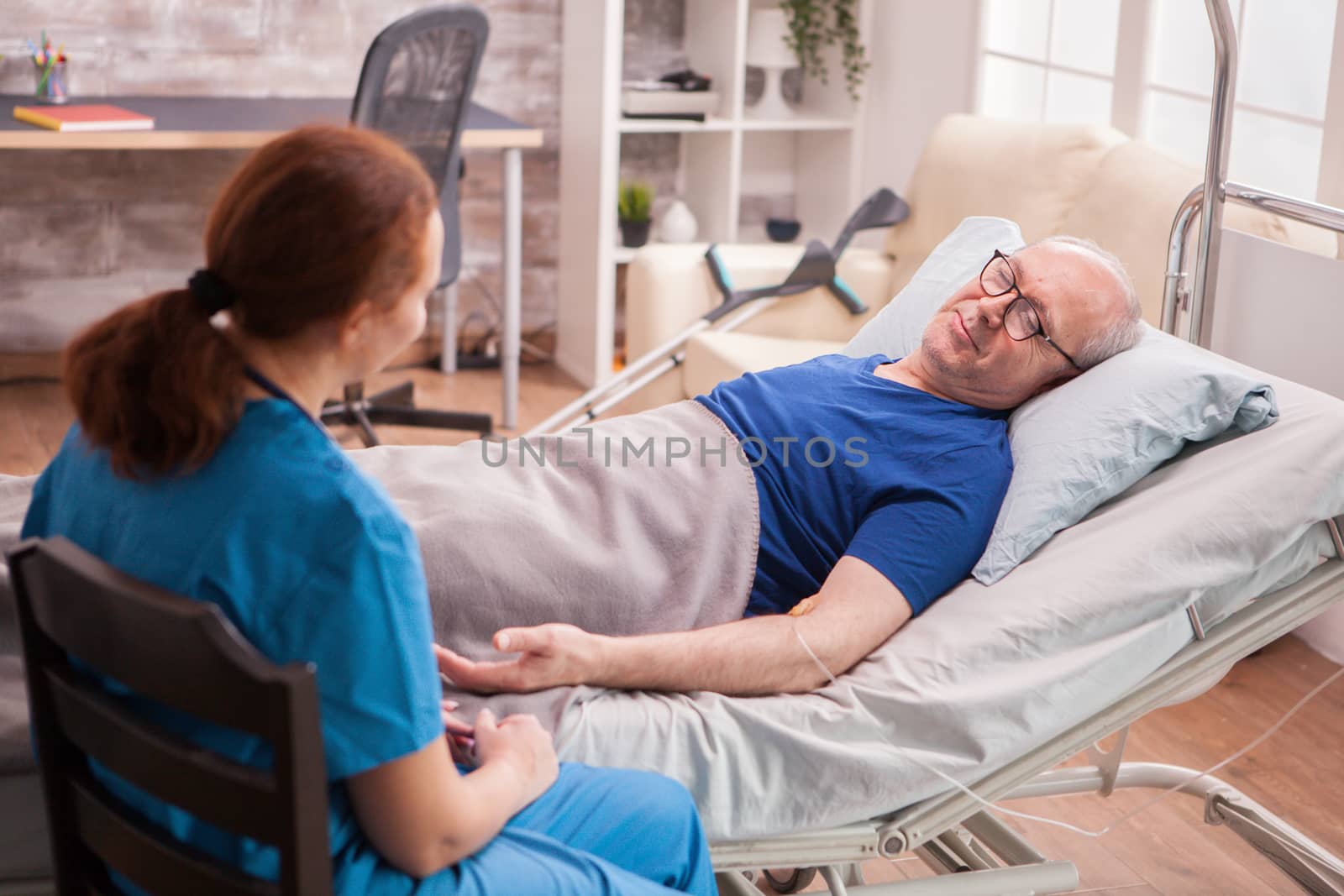 Back view female doctor in nursing home sitting next to old man lying in bed.