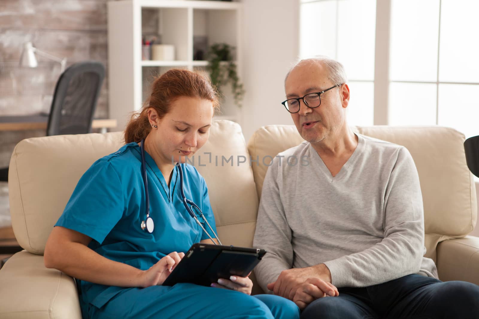 Female nurse in nursing home helping old man to use tablet computer.