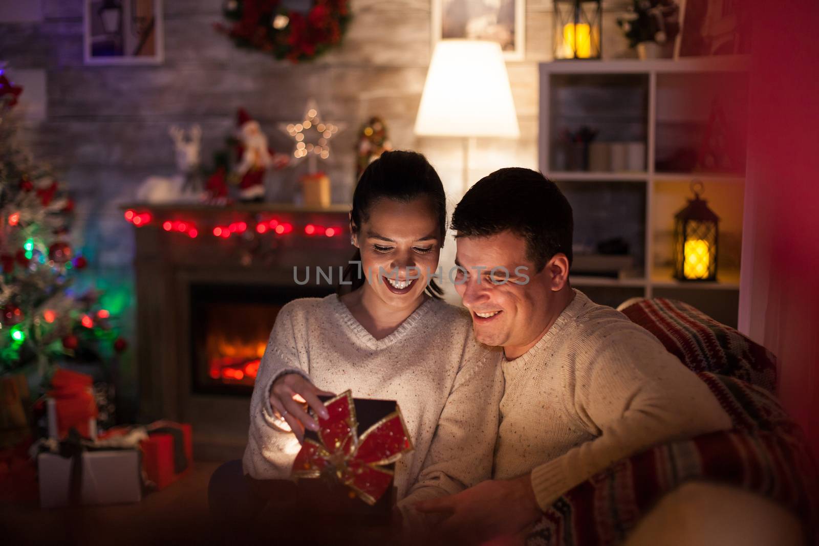 Young woman with magical gift from husband on christmas day with fireplace and christmas tree in dark living room.