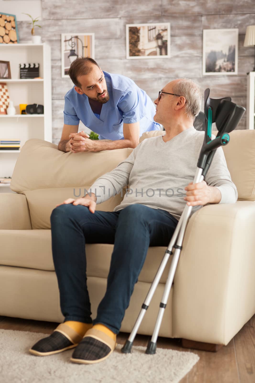 Male doctor with stethoscope in nursing home talking with old man. Man with crutches.