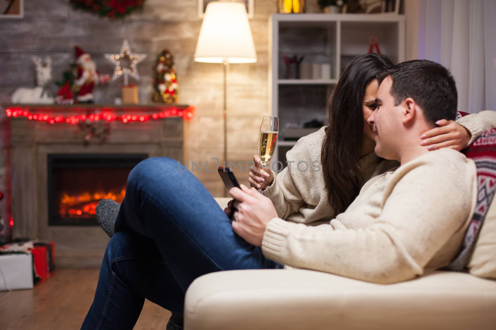 Beautiful woman holding a glass of wine and whispering something to her husband celebrating christmas.
