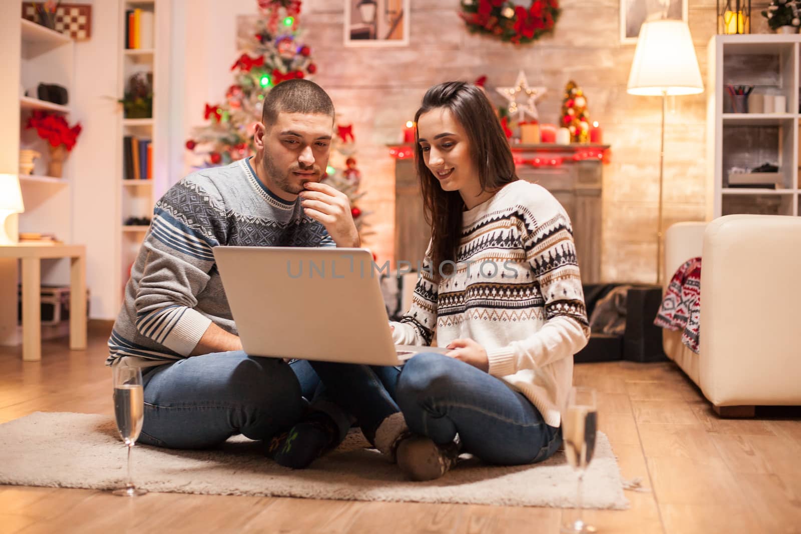 Happy couple in matching clothes doing online shopping for christmas on laptop.