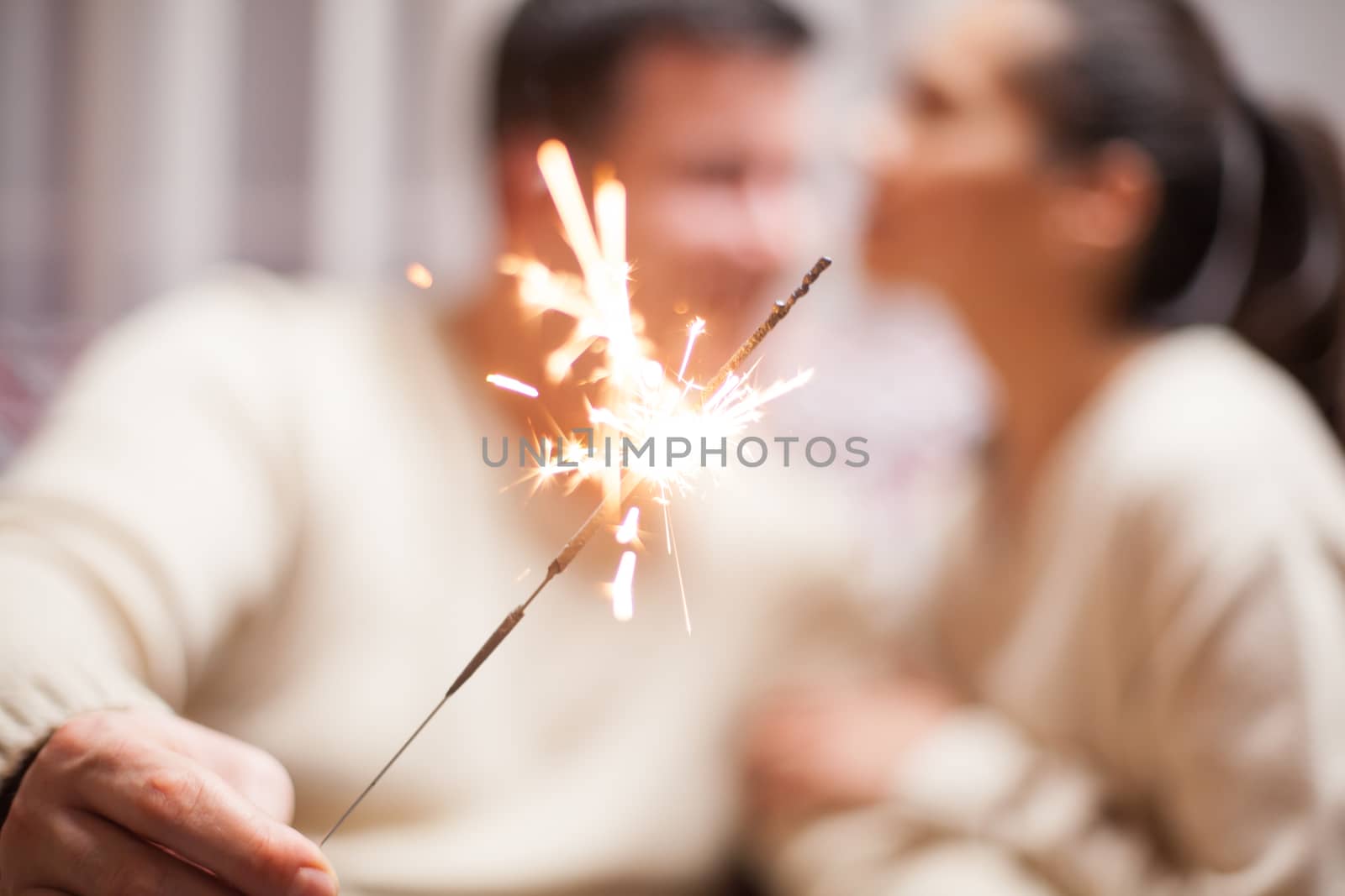 Blurred couple holding bengal light on christmas day sitting on couch with matching clothes.