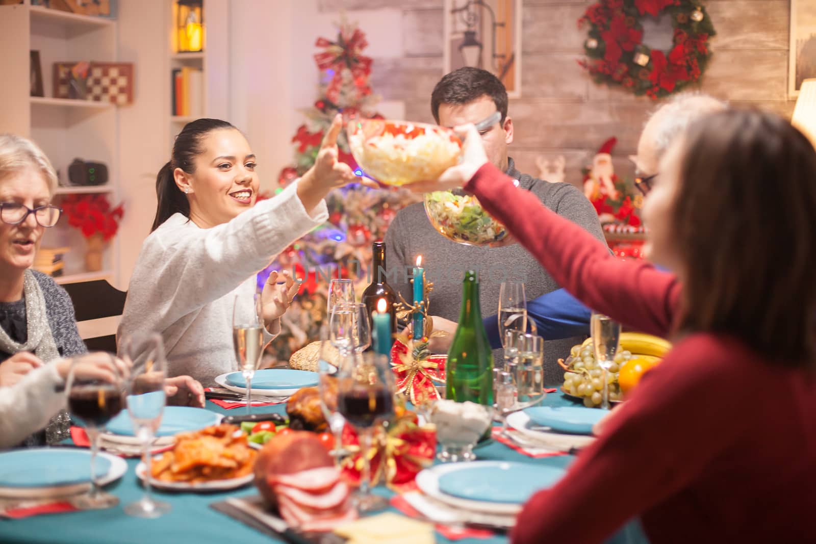 Happy woman passing the salad over the table to his daughter at christmas family dinner.