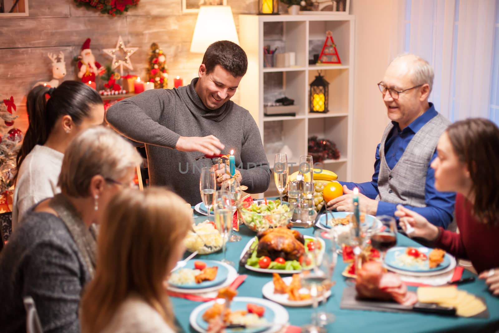 Cheerful young man opening a bottle of wine at christmas family dinner.