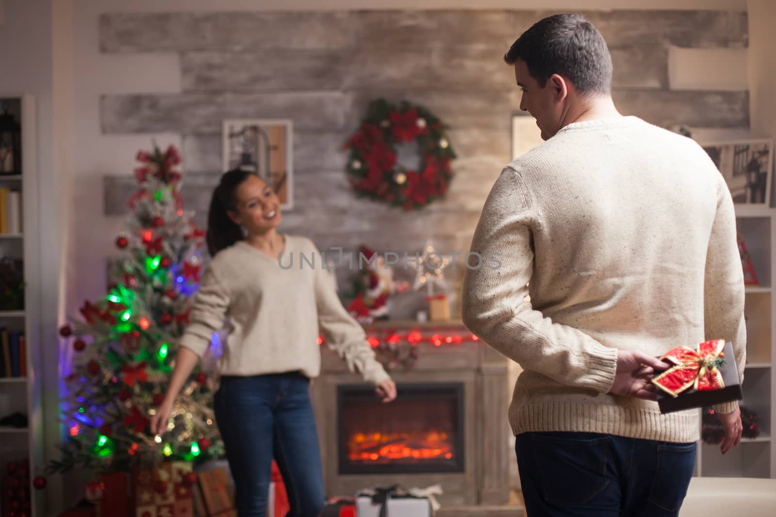 Young man holding a gift behind him for his girlfriend on christmas day wearing matching clothes.