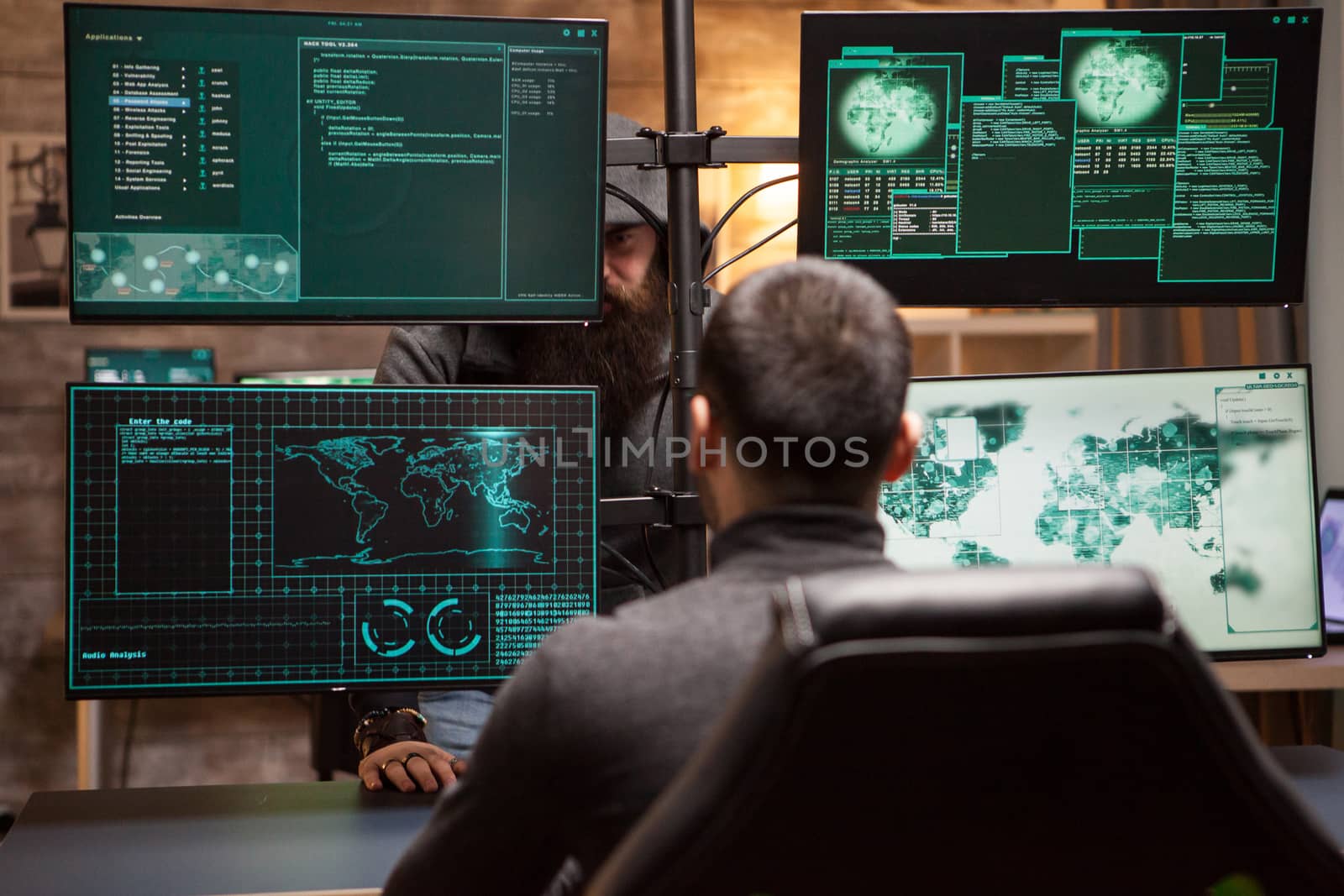 Bearded old hacker wearing a hoodie talking with young hacker about new cyber attack.
