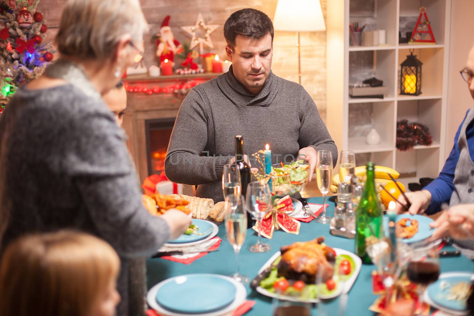 Happy father putting some salad in his plate at christmas family dinner.