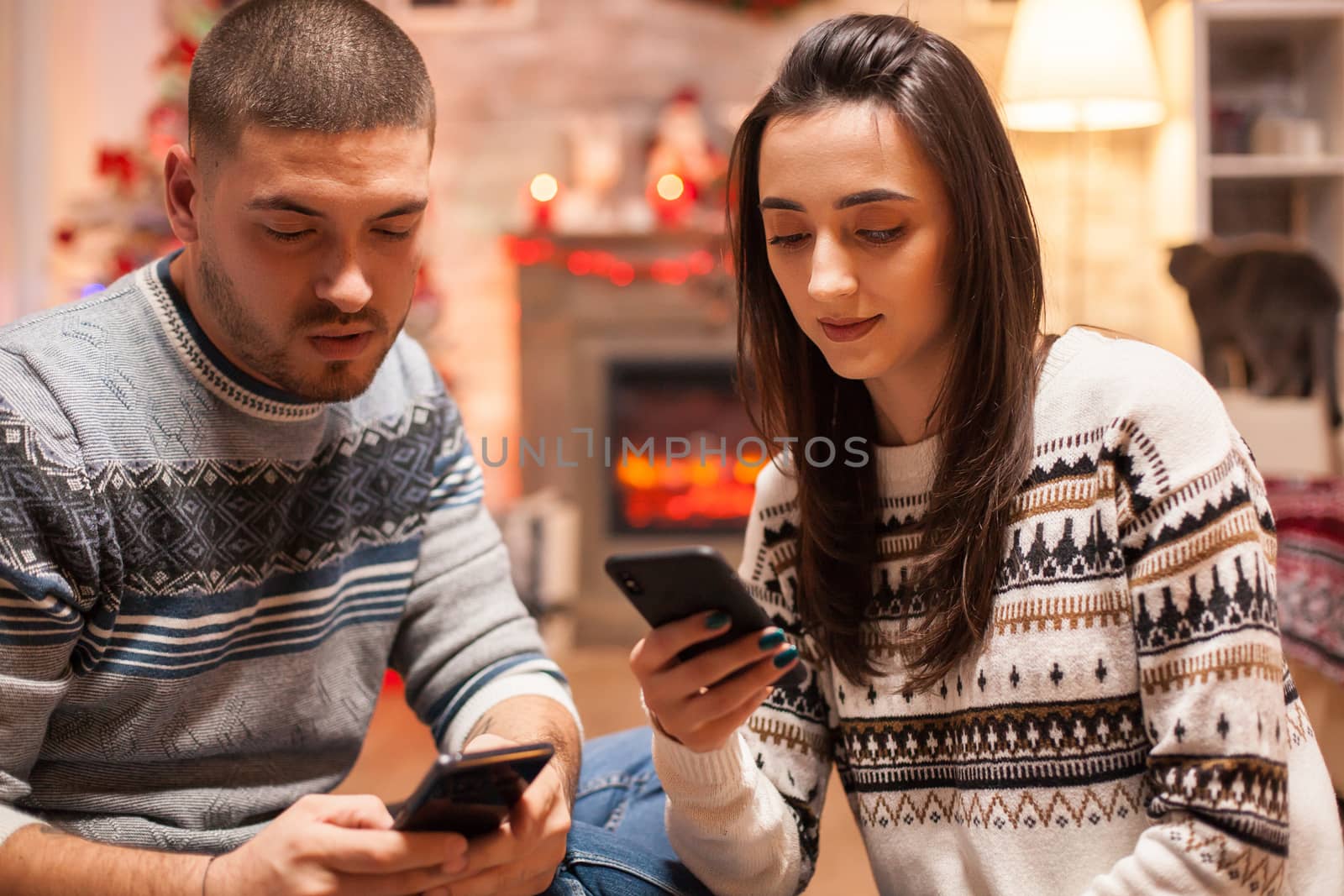 Loving couple on christmas day wearing matching clothes browsing on smartphone.