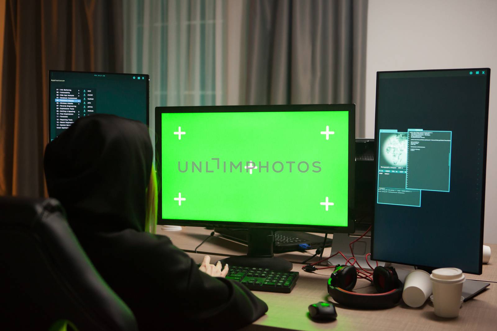 Shot from behind of female hacker writing a virus on computer with green screen.