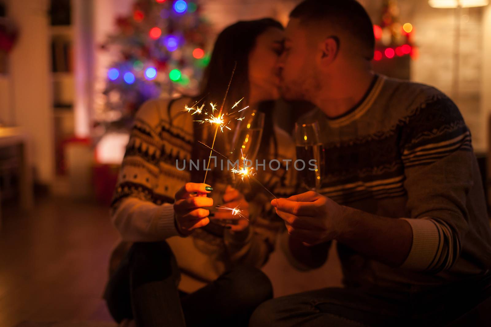 Couple kissing in dark room holding burning hand fireworks on christmas day.