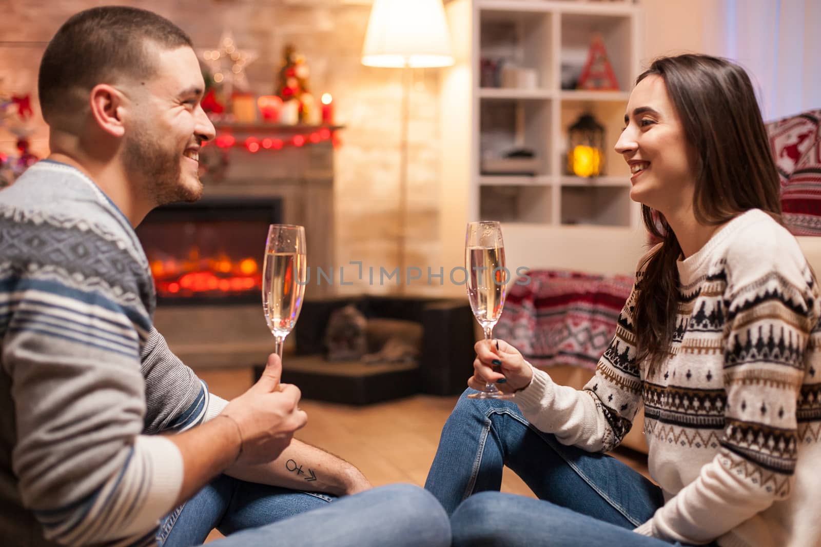 Cheerful boyfriend and girlfriend with a big smile clinking a glass of champagne on christmas day. .